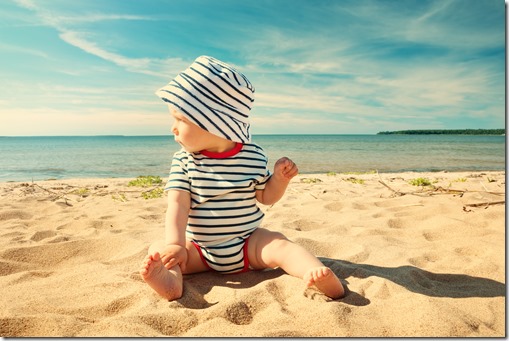 Little baby boy sitting on the beach in summer day